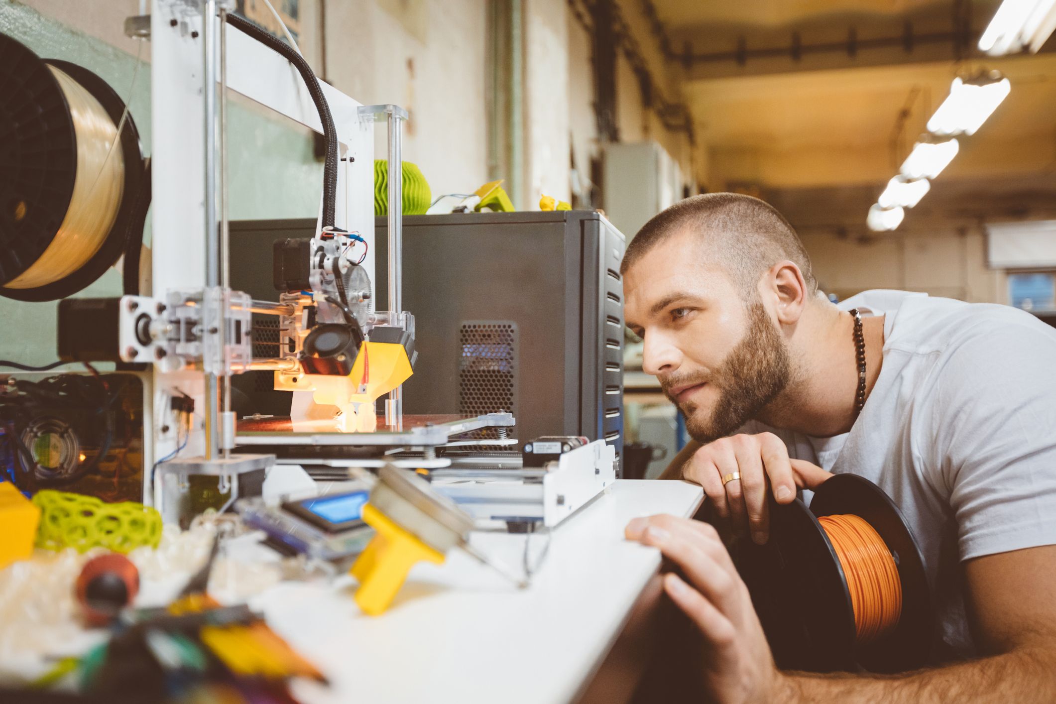 Junger Mann, der sich einen 3D-Drucker bei der Arbeit anschaut