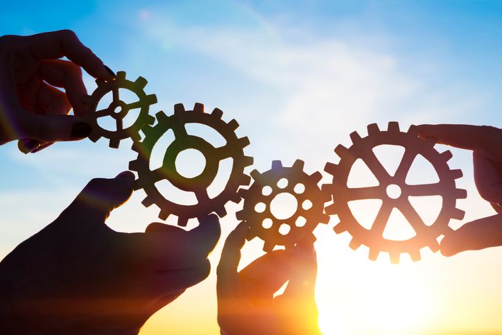 Hände, die Zahnräder halten, welche ineinander greifen